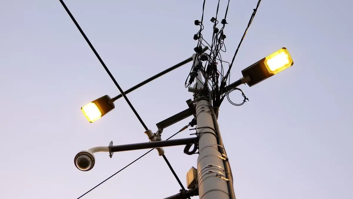 Poste de iluminação pública com duas luminárias acesas ao anoitecer